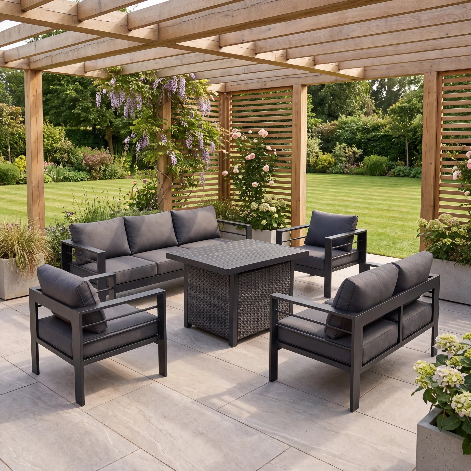 A 5-piece outdoor patio dining set with a dark gray wicker-look table and matching armchairs and sofa, arranged on a paved patio under a wooden pergola with a lush garden background.